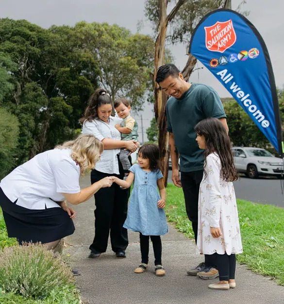 A Salvation Army officer warmly greeting a family of five on a path.