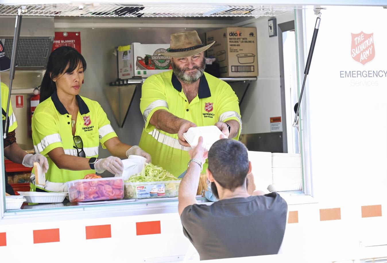 Two Salvation Army Emergency Services workers serve food and drink from the Food Truck window