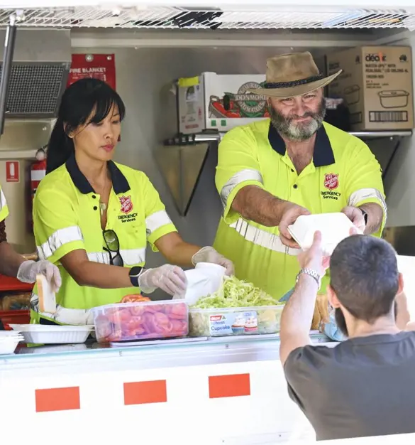 Two Salvation Army Emergency Services workers serve food and drink from the Food Truck window